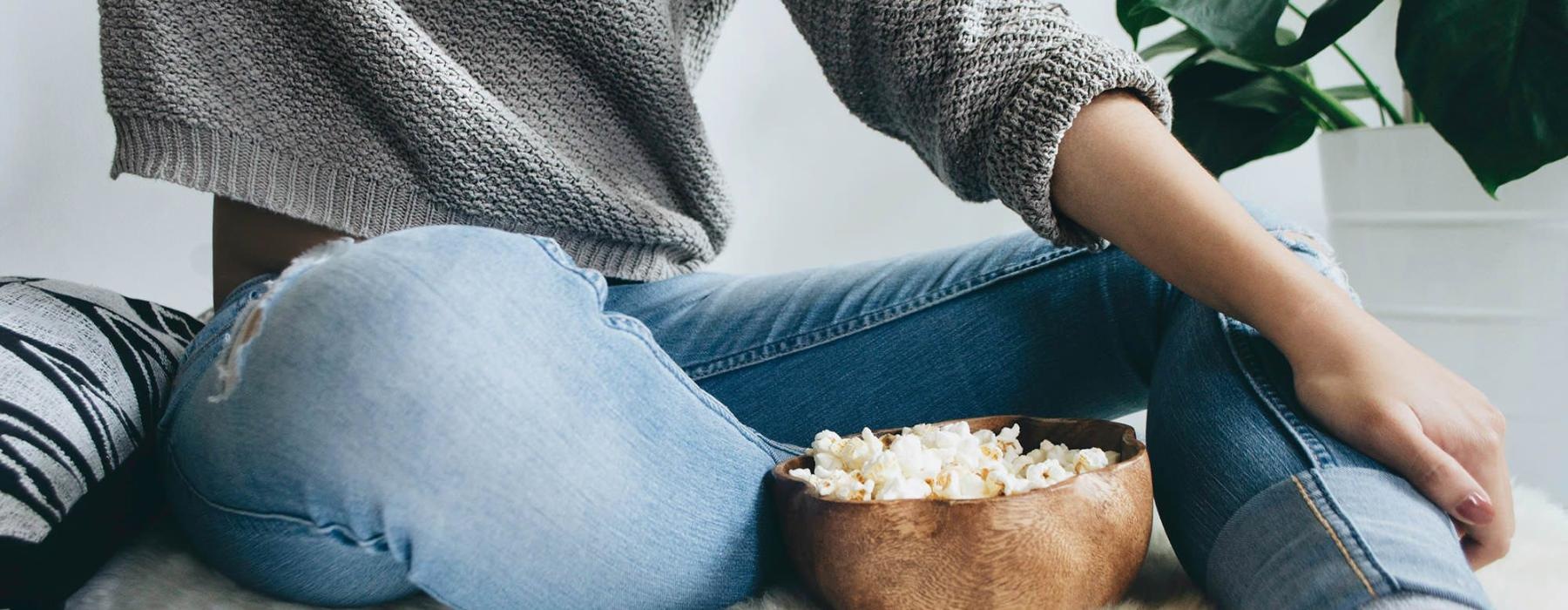 woman sits on a rug with a bowl of popcorn