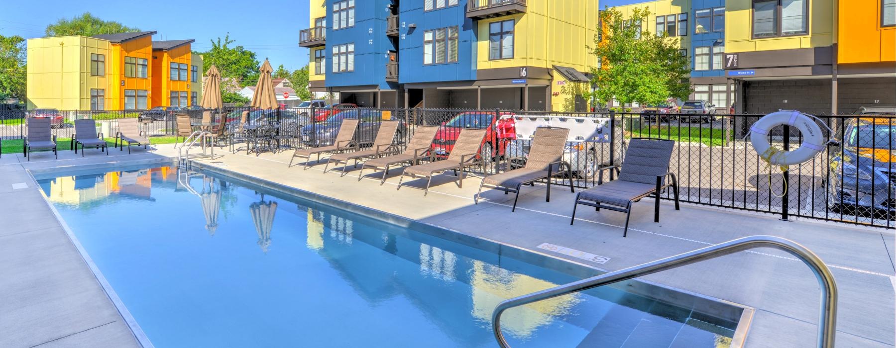 a pool with chairs and tables by it and buildings around it