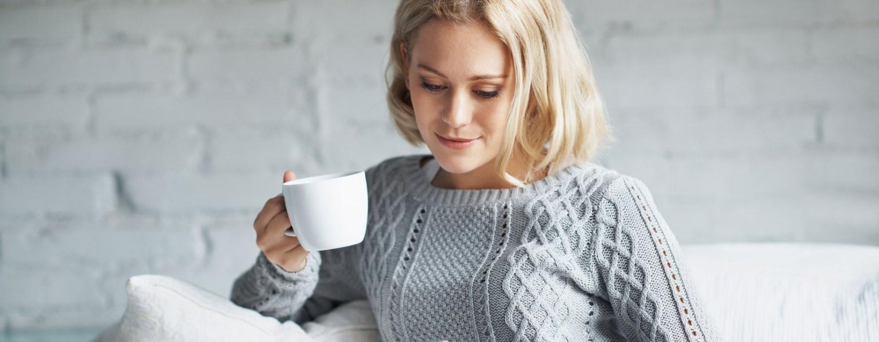 a woman sits on a couch with a cup of coffee and looks at her tablet